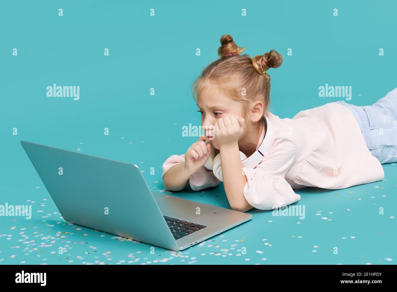 Bambina intelligente che usa un computer portatile su sfondo ciano. Formazione, studio online, tv, apprendimento a distanza. Studente della scuola primaria durante la quarantena. Istruzione Foto Stock