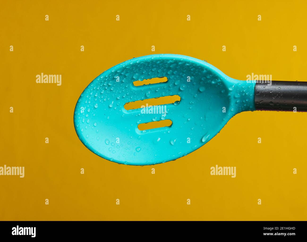 Cucchiaio da cucina in silicone colander in gocce d'acqua su sfondo giallo Foto Stock