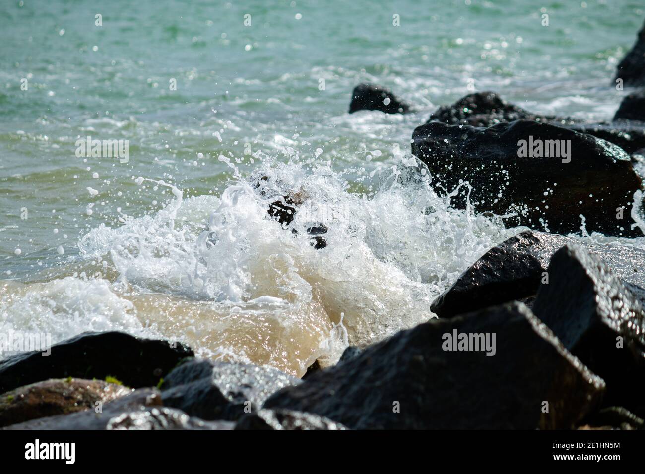 le onde dell'oceano si infrangono sulle rocce sulla spiaggia, l'acqua di mare limpida si rompe in schiuma bianca. Foto Stock