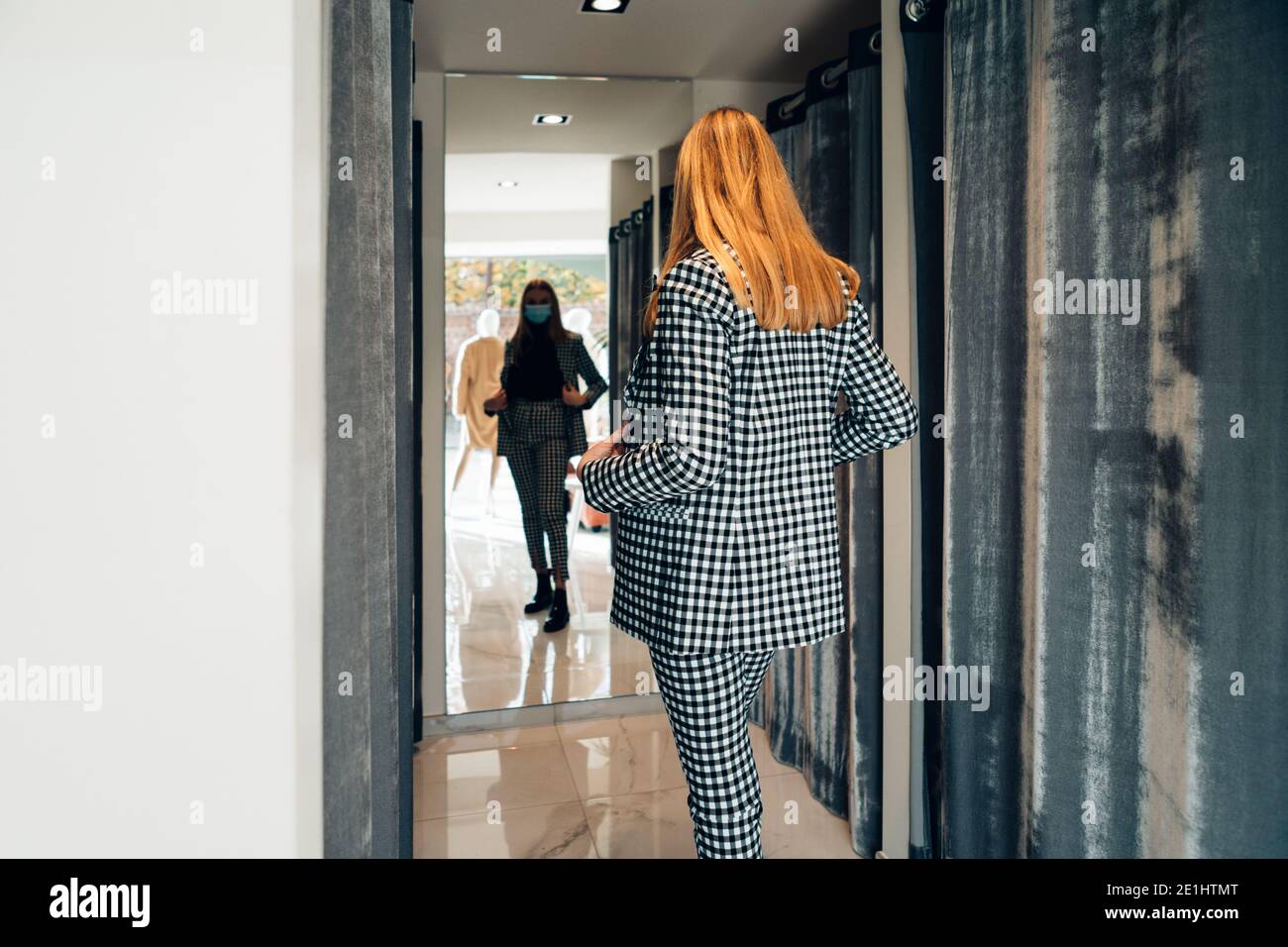elegante giovane bionda caucasica in un negozio di moda indossare un abito mentre si guarda nello specchio Foto Stock