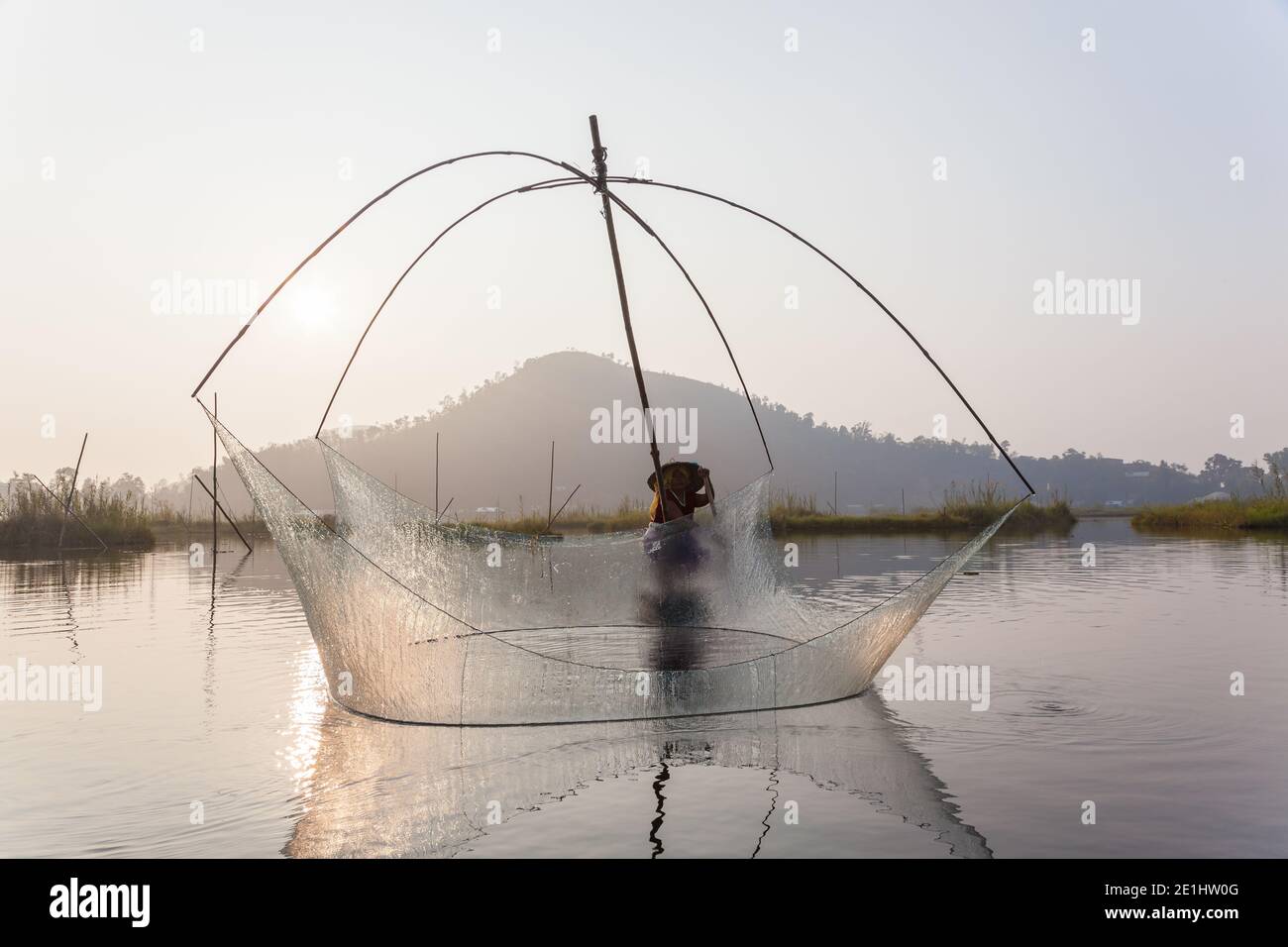 Il pescatore sulla sua barca che muove le reti oscillanti ad arco sopra il Acqua al lago Loktak Foto Stock