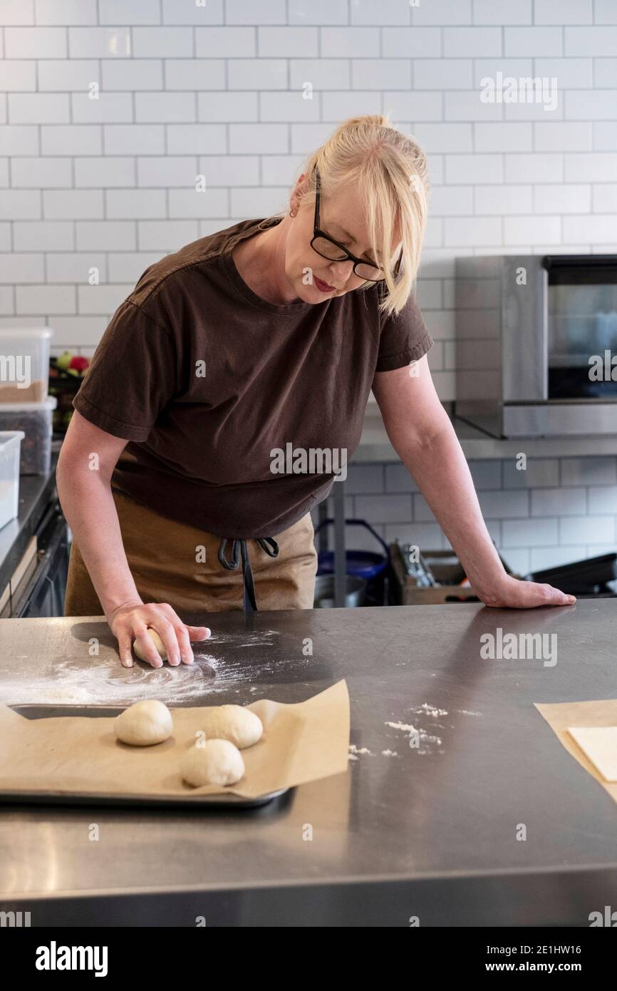 Donna in grembiule marrone in piedi in una cucina di caffè, mescolando pasta pasticceria danese Foto Stock