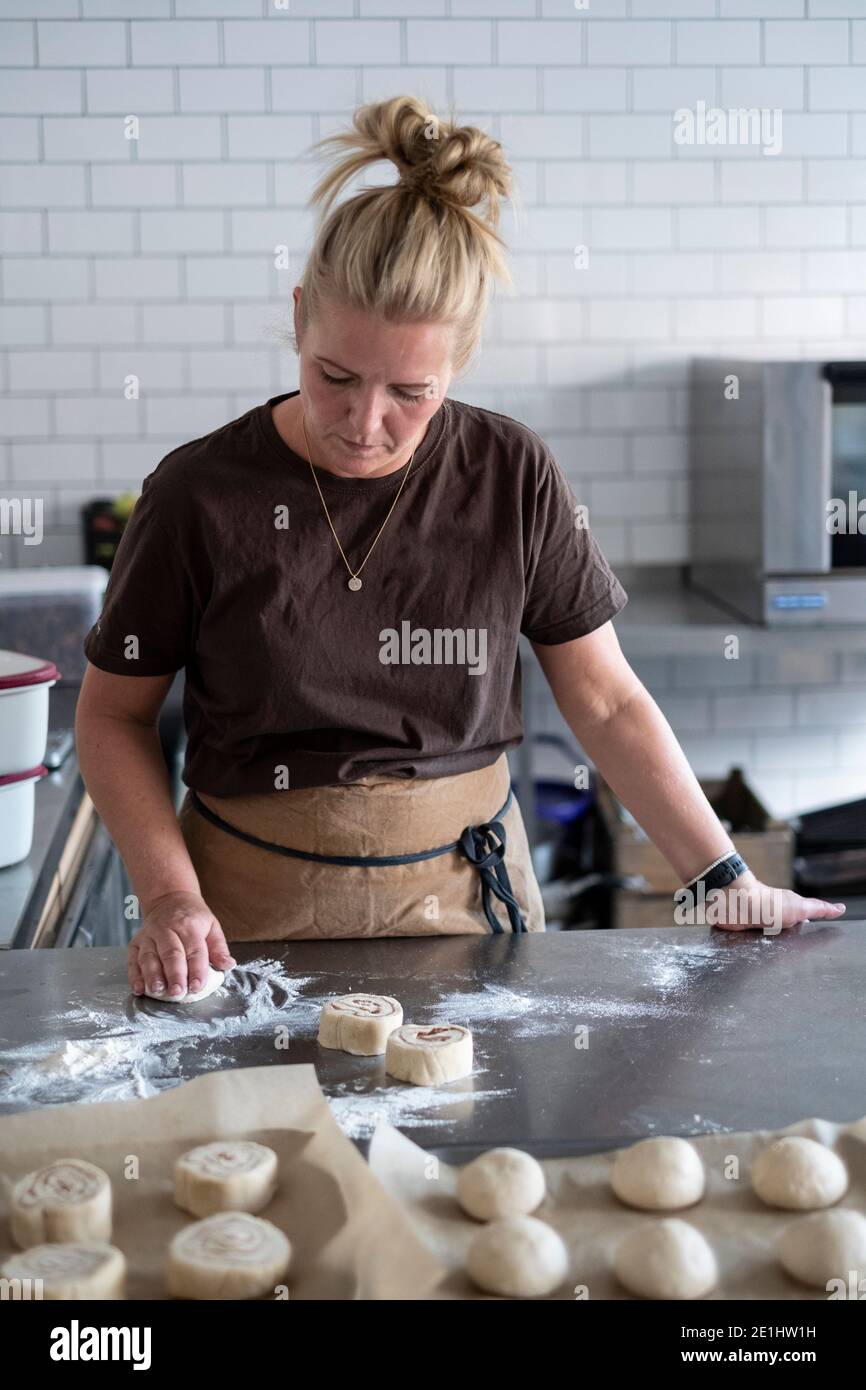 Donna bionda che indossa grembiule marrone in piedi in una cucina, che cuoce pasticceria danese. Foto Stock