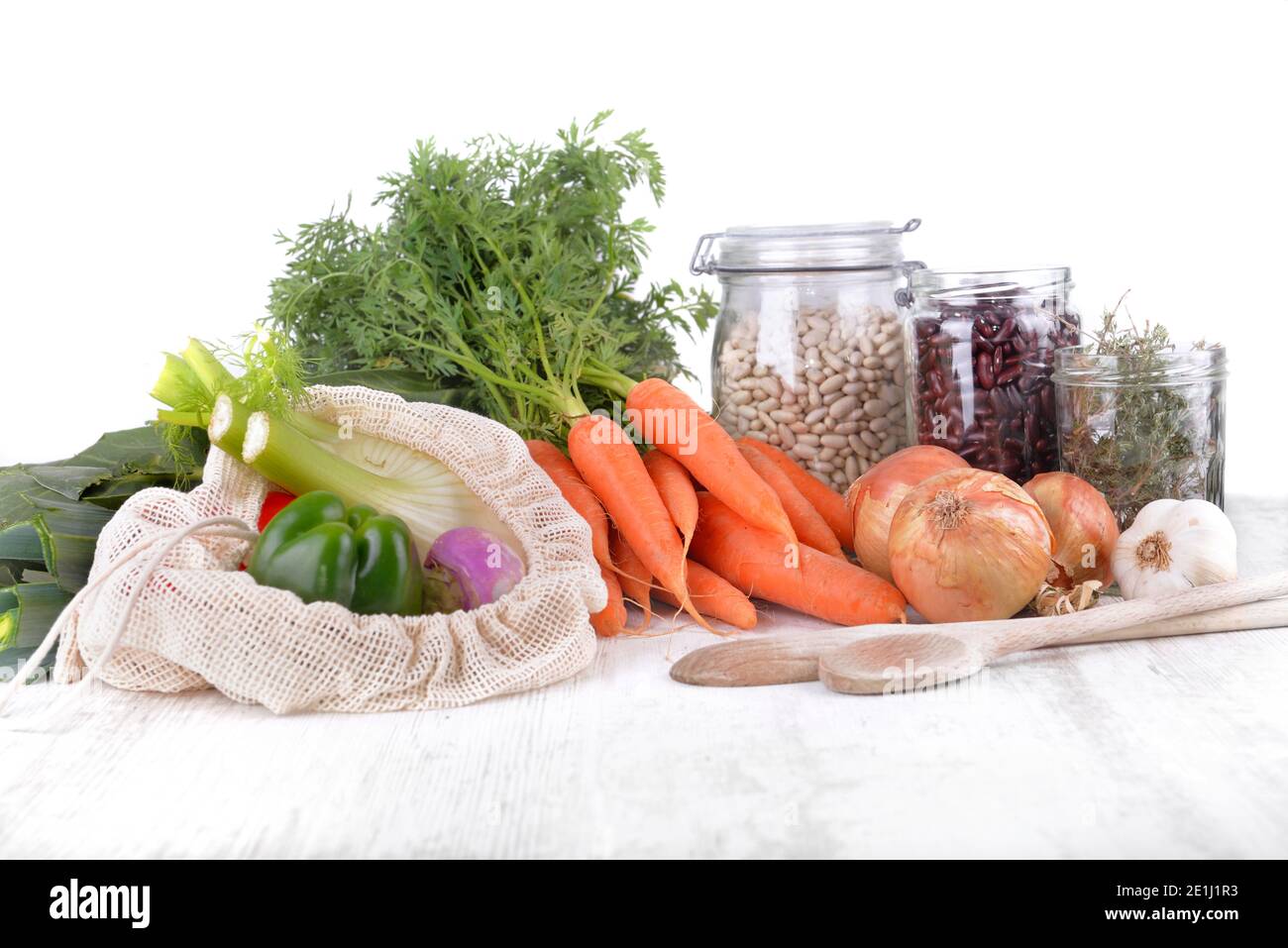 verdure fresche in un sacchetto riutilizzabile e fagioli secchi dentro vasetto con cipolle e aglio su un tavolo bianco sfondo Foto Stock