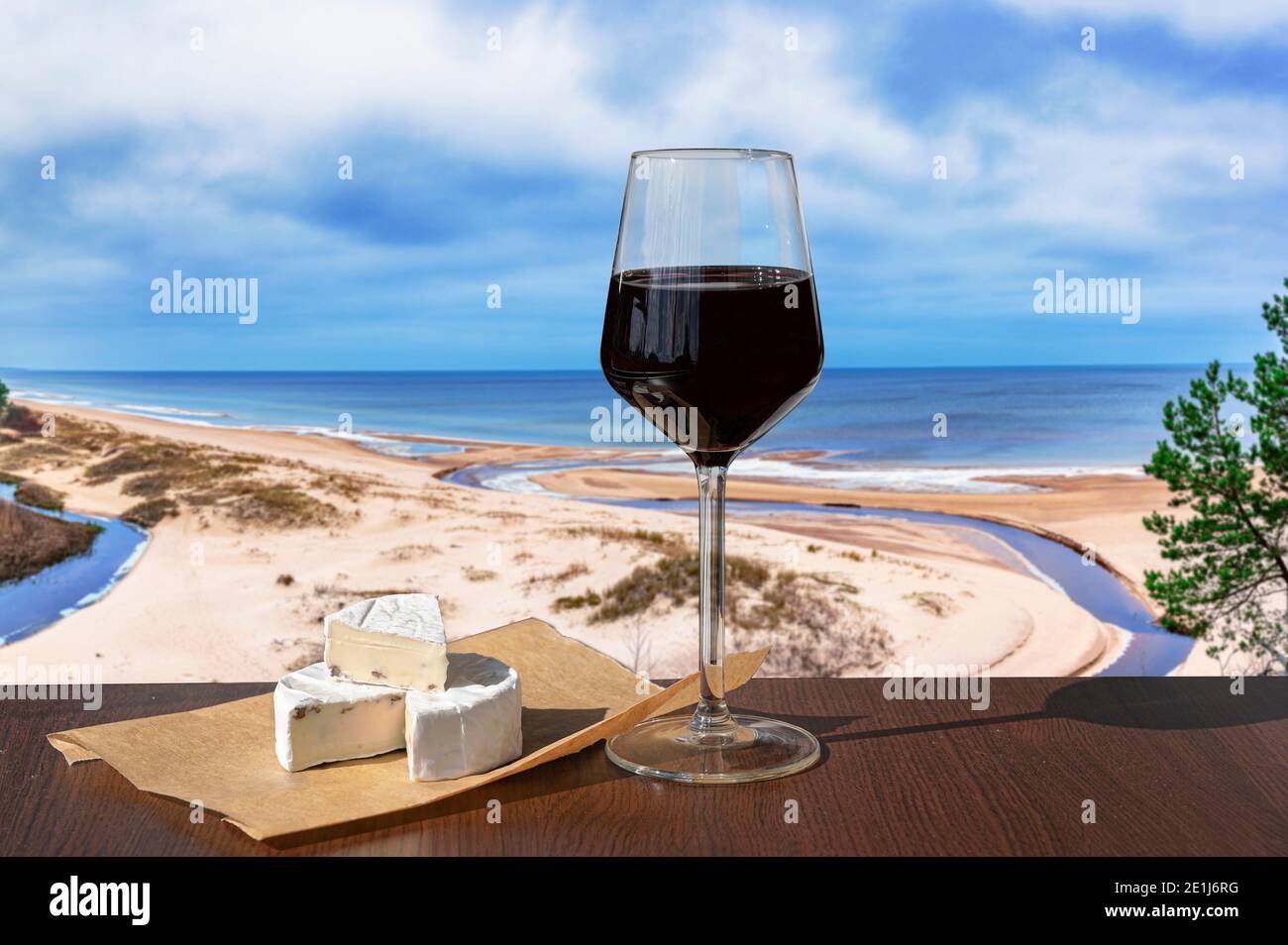 Bicchiere di vino rosso con formaggio brie con vista sulla spiaggia e sul Mar Baltico. Spiaggia con sabbia bianca, pineta e mare blu o oceano. Foto Stock