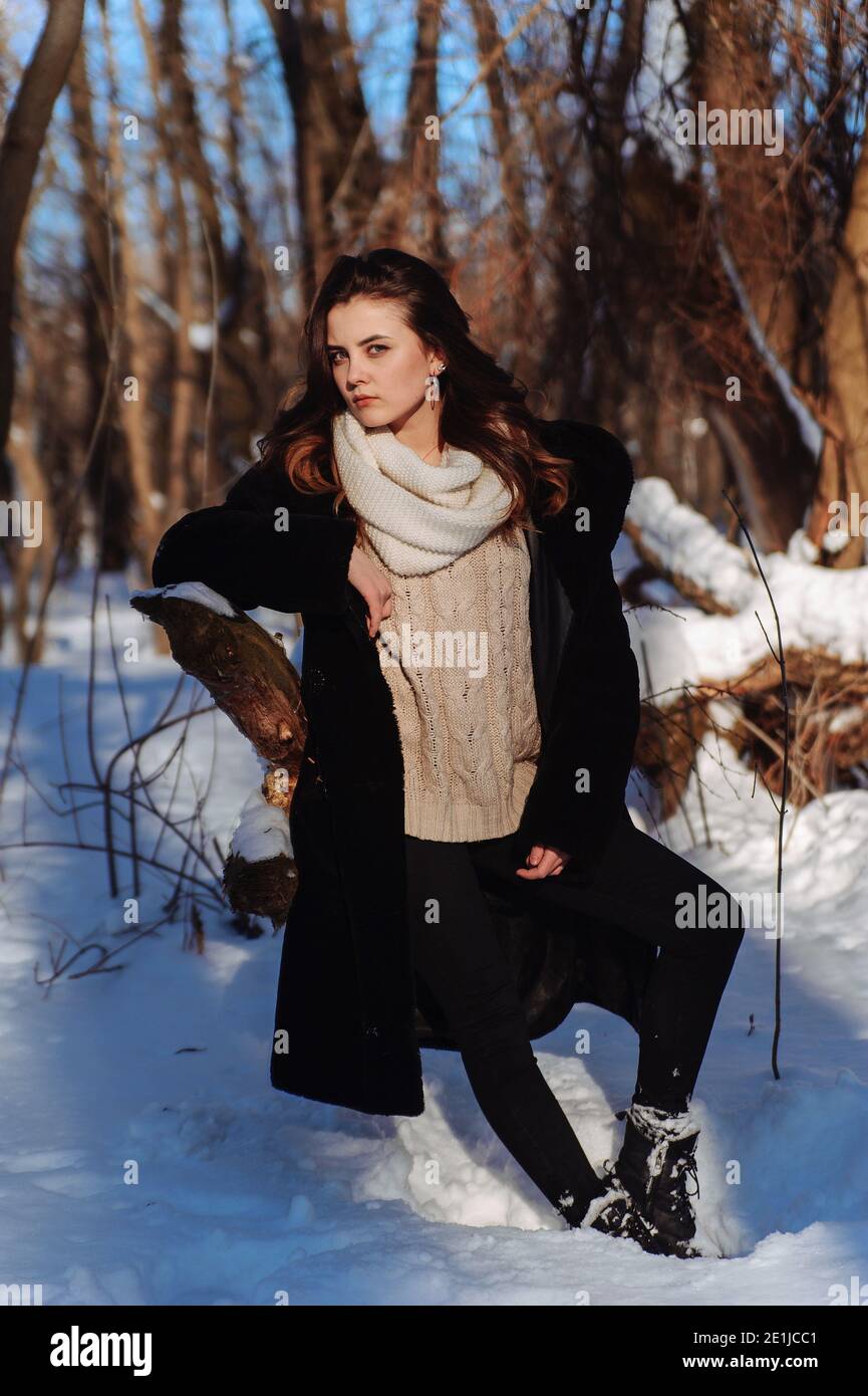 Ragazza seria nel cappotto nero e sciarpa bianca appoggiata sul ramo  dell'albero nella foresta d'inverno. Giornata invernale soleggiata Foto  stock - Alamy