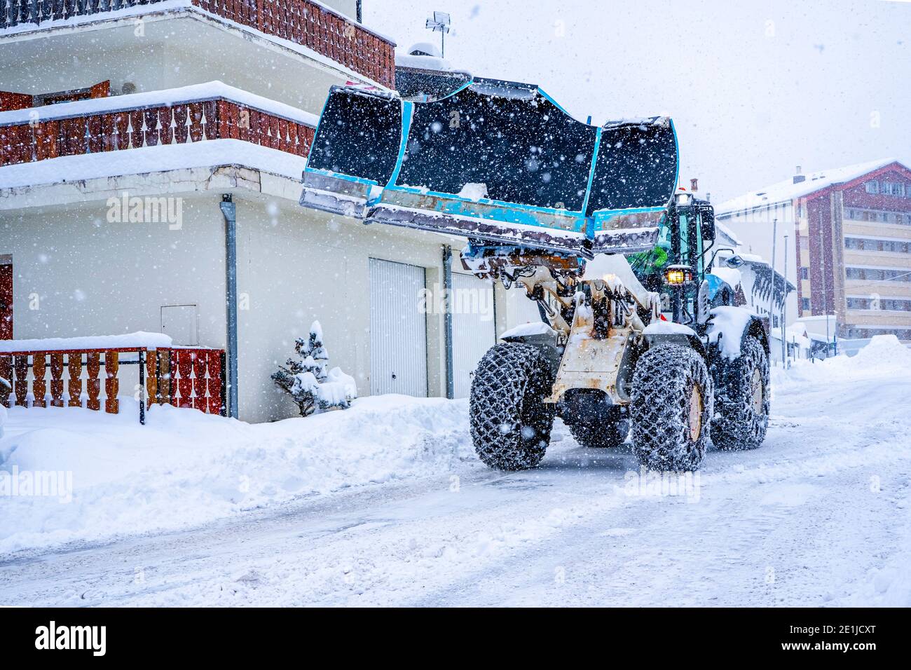 Trattore che rimuove la neve dalle grandi rive della neve vicino alla strada su una stazione sciistica nelle Alpi francesi. Foto di alta qualità Foto Stock