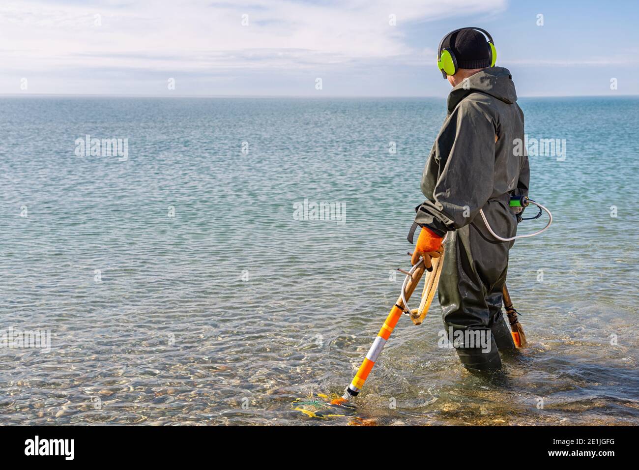 Un uomo in piedi ginocchio-profondo nell'acqua alla ricerca di metalli  preziosi con un metal detector. Mare e cielo sullo sfondo. Storia e  concetto di archeologia Foto stock - Alamy