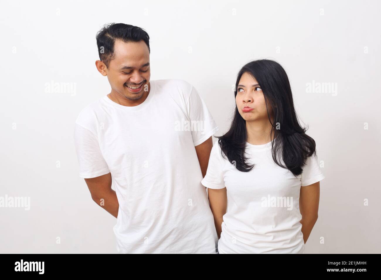 Accigliata donna carina mentre guarda il suo ragazzo. Coppia asiatica in camicia bianca isolata su sfondo bianco con copyspace Foto Stock