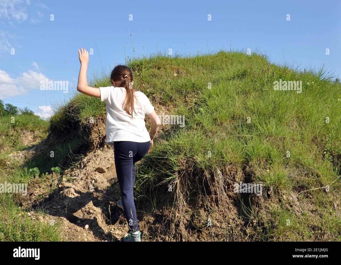 Bambino, ragazza bionda con capelli lunghi, scalando una piccola collina con erba verde, dorso Foto Stock