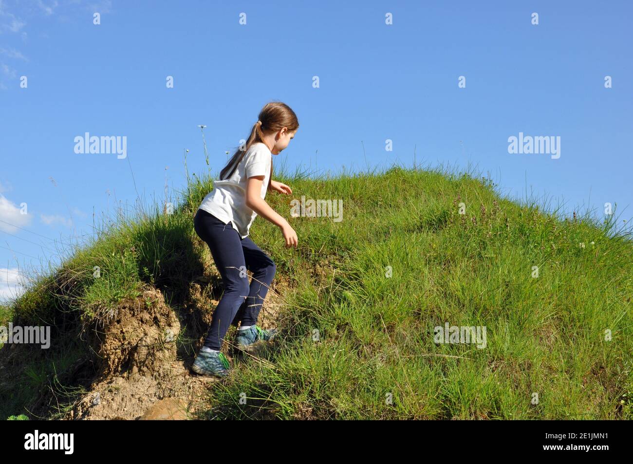 Bambino, ragazza bionda con capelli lunghi, arrampicandosi su una piccola collina con erba verde Foto Stock