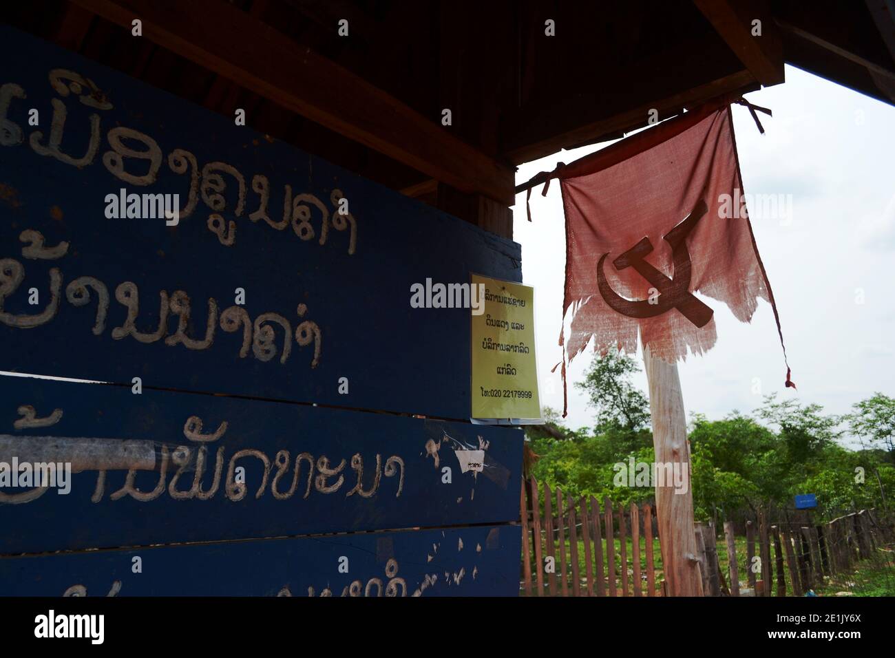 Konglor, Loas - Aprile 2015: Straccio di bandiera comunista su una vecchia fermata dell'autobus lungo la strada. Simbolo del comunismo nel piccolo villaggio del Laos Foto Stock