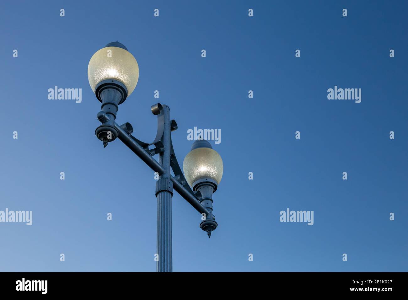 Un lampione della città è visto da un angolo basso contro un cielo blu sfumato. Le luci sono illuminate in un telaio in vetro foggato sopra un supporto in metallo blu. Foto Stock