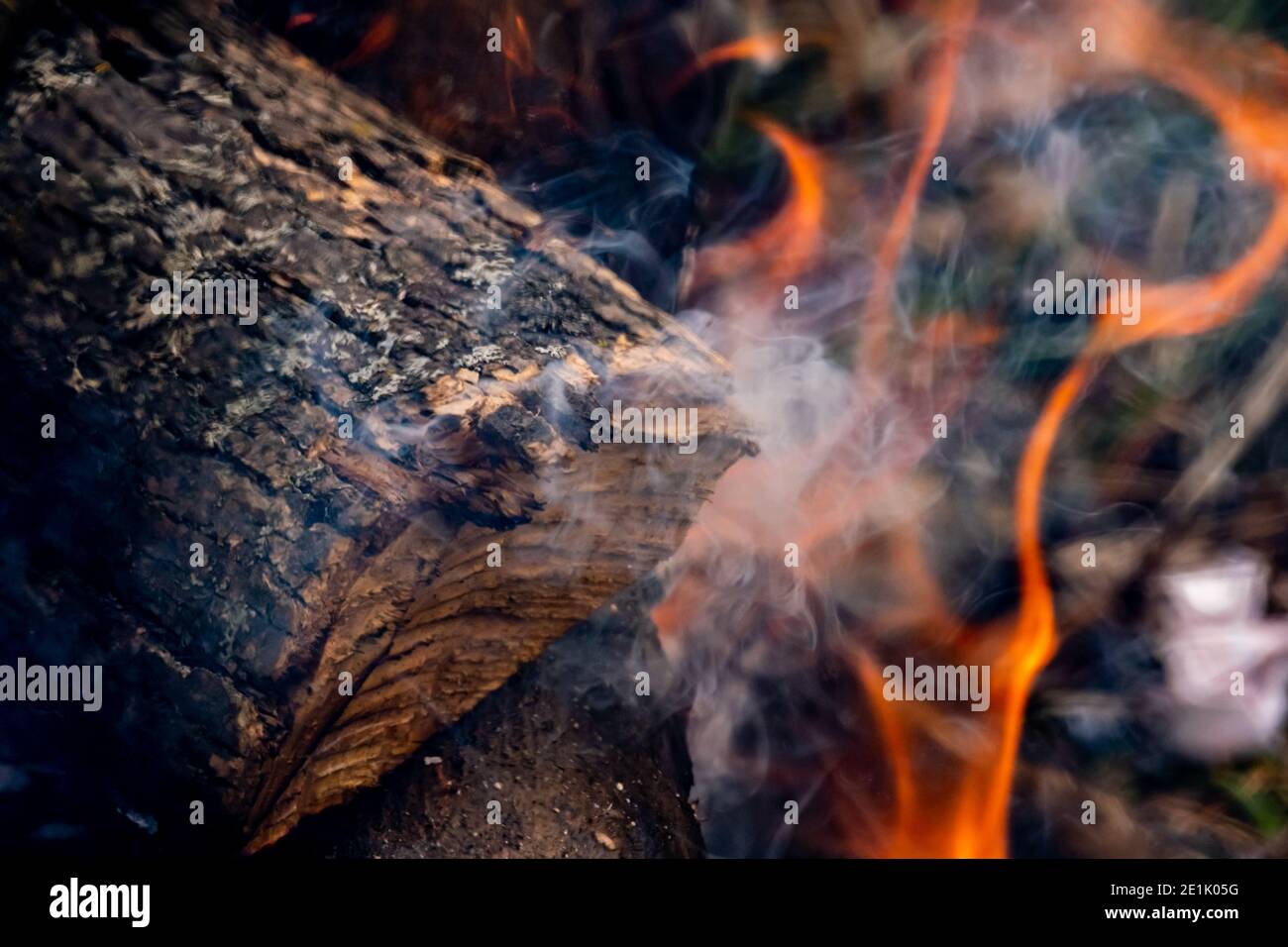 Un ceppo di legno tagliato è fumare con le fiamme sotto di esso in un falò esterno in una vista ravvicinata. Foto Stock