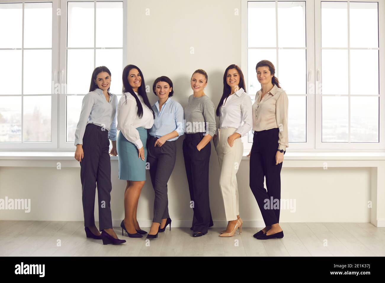 Squadra di donne felici di affari che stanno insieme in nuovo ufficio e sorridendo alla macchina fotografica Foto Stock