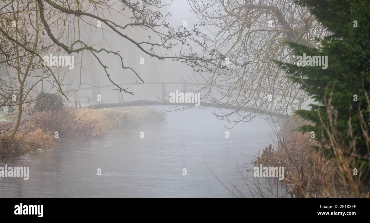 Ponte di legno sul piccolo fiume visto attraverso una forte nebbia in un giorno di inverni Foto Stock