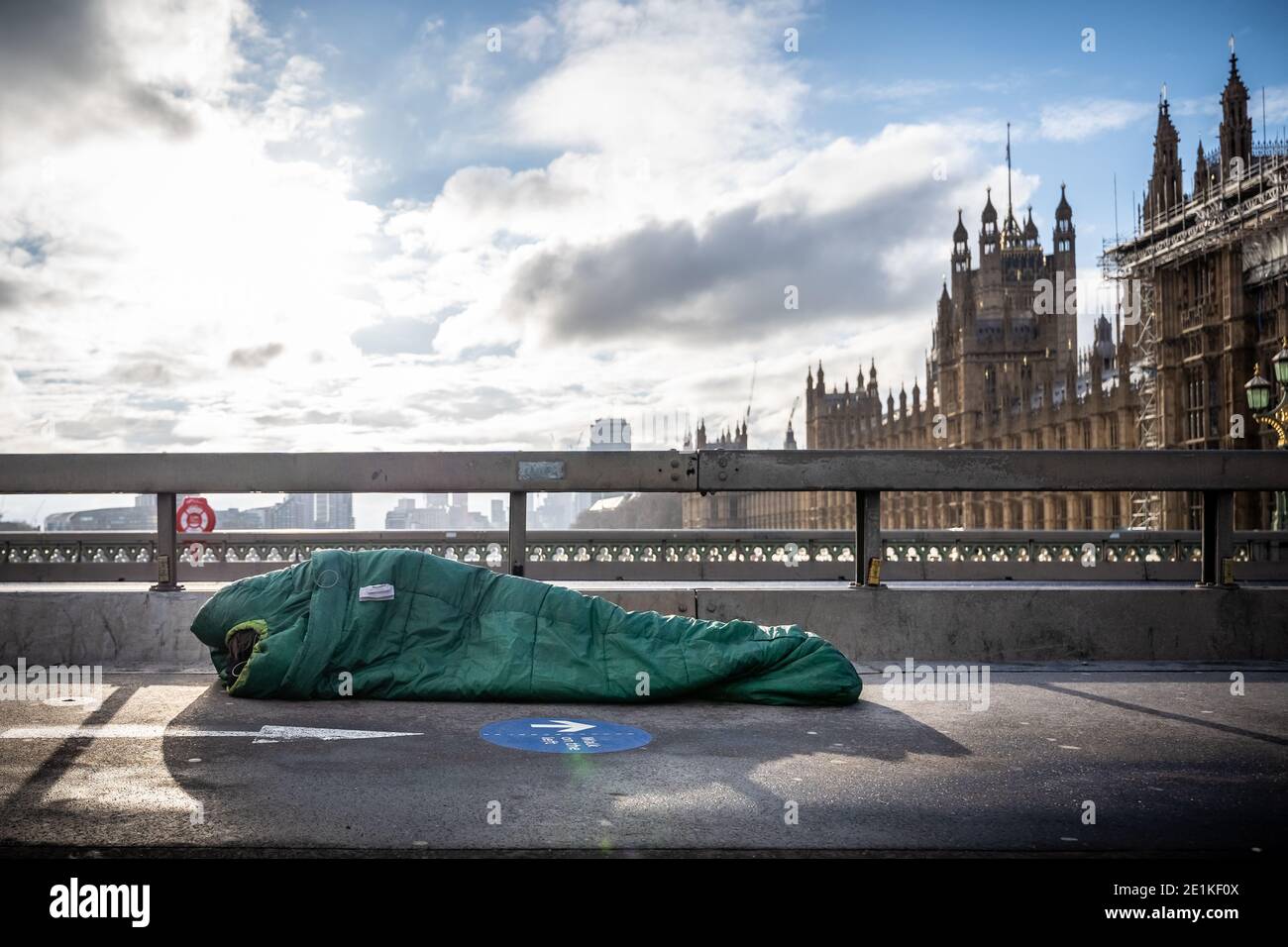 Un sonno sconnesso nel suo sacco a pelo a mezzogiorno su Westminster Bridge, Londra, Regno Unito. Foto Stock