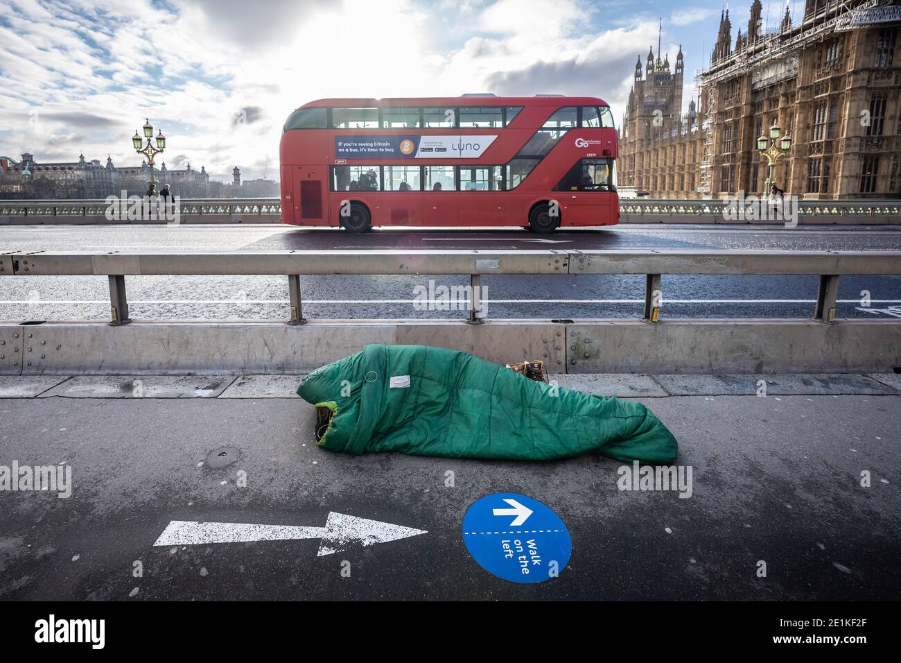 Un sonno sconnesso nel suo sacco a pelo a mezzogiorno su Westminster Bridge, Londra, Regno Unito. Foto Stock