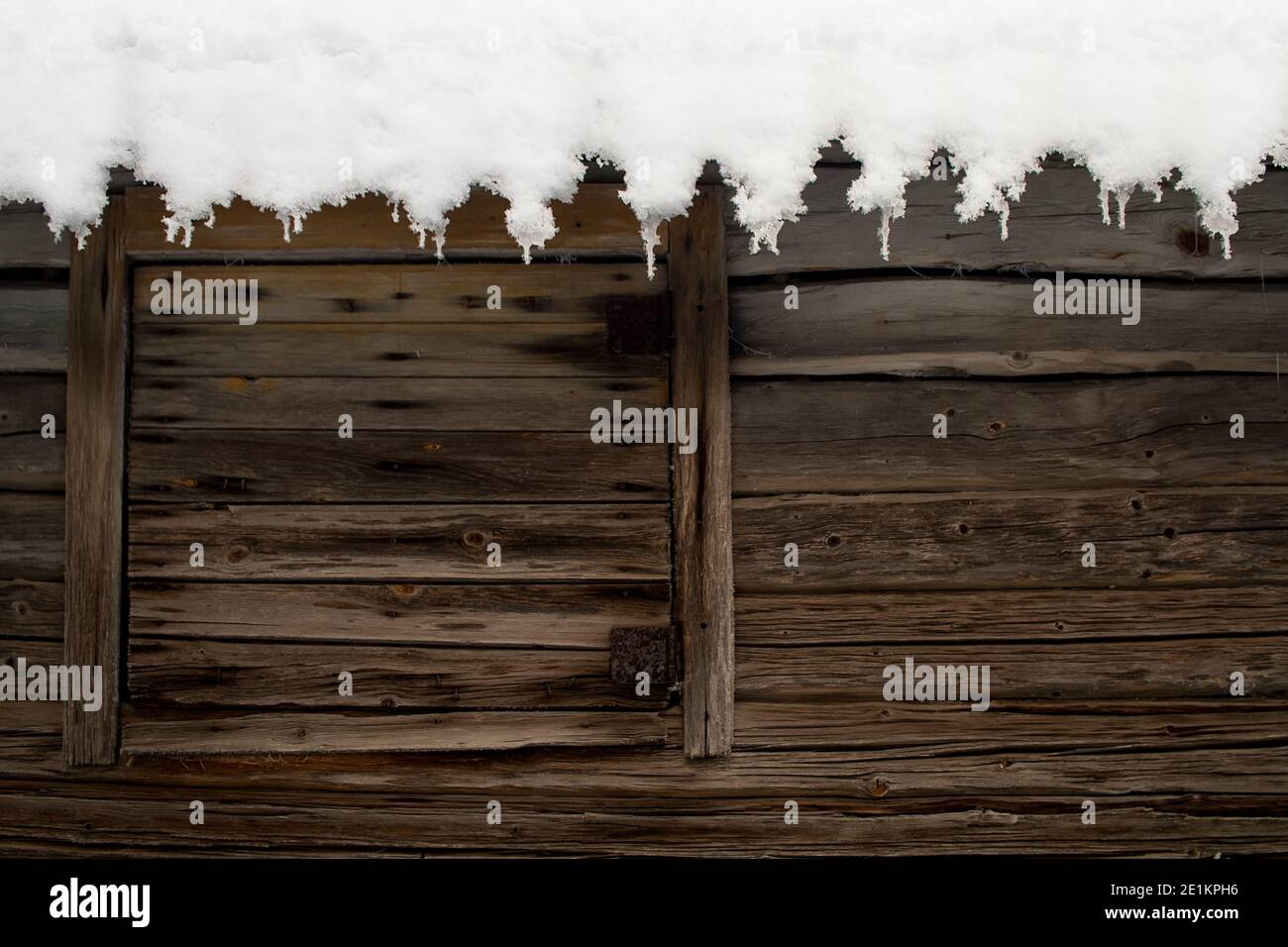 La neve copre il tetto di un vecchio edificio agricolo. Il sole sta sciogliendo la neve e sta formando belle iciclette al bordo del tetto. Foto Stock