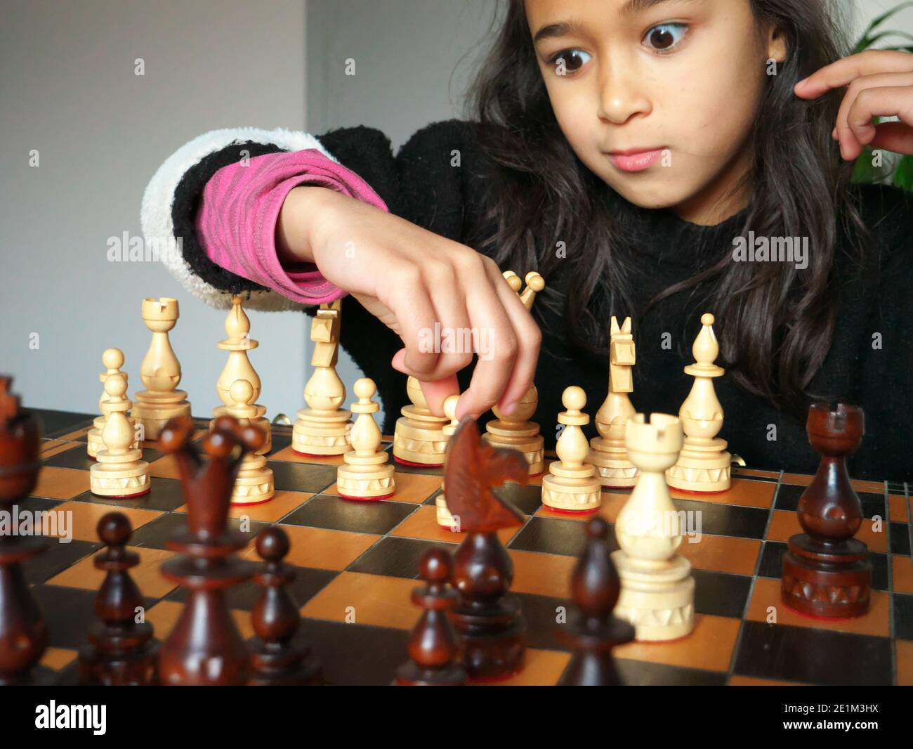 Bambina che gioca a scacchi con uno sguardo sorpreso sul viso. Foto Stock
