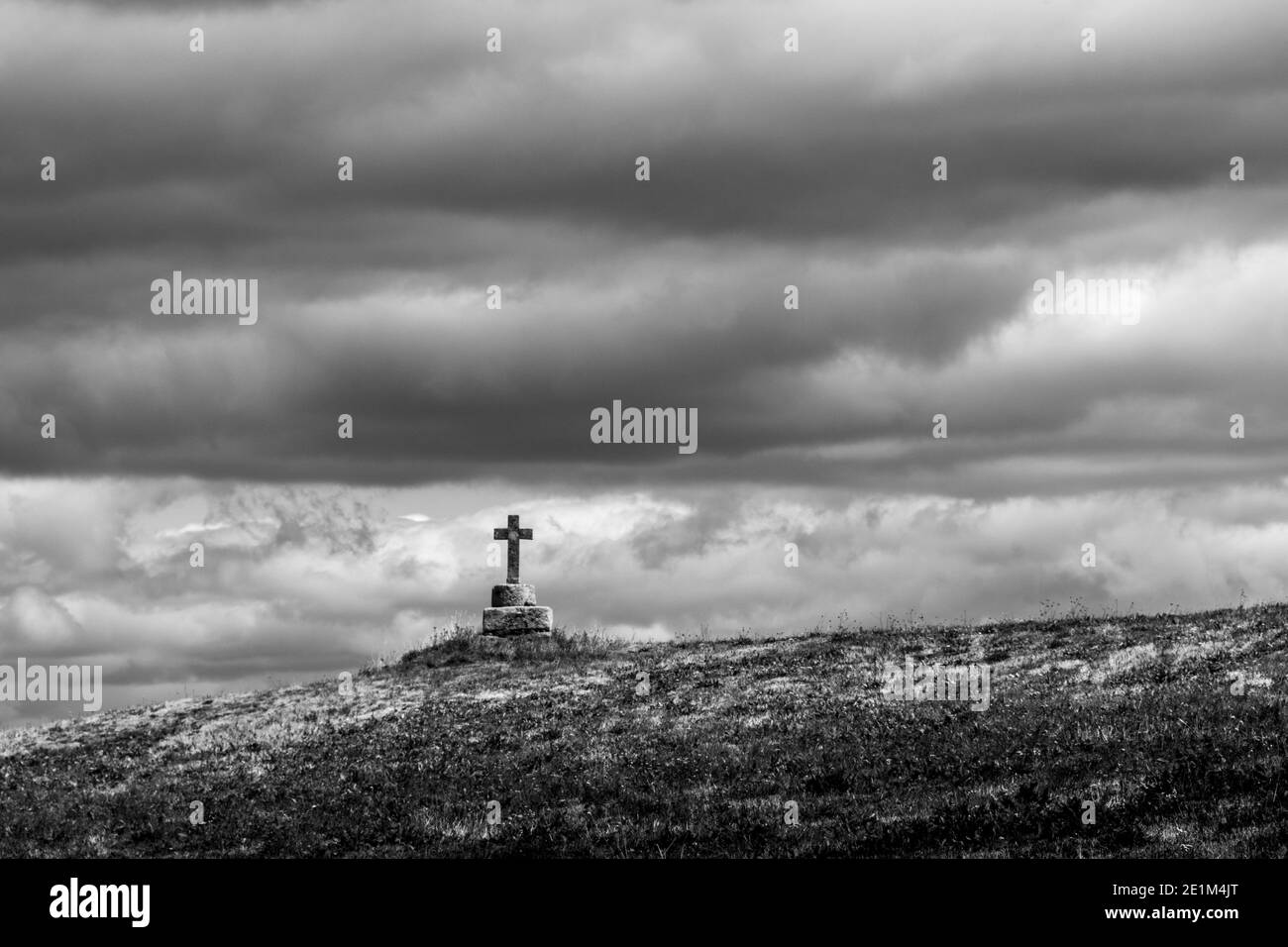 Paesaggio monocromatico caratterizzato da una croce solitaria su una collina sotto spettacolari nuvole durante il tempo coperto in Alvernia. Francia Foto Stock