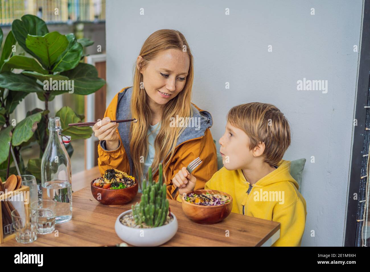 Madre e figlio mangiano il ciotola di poke organico crudo con riso e verdure primo piano sul tavolo. Vista dall'alto orizzontale Foto Stock