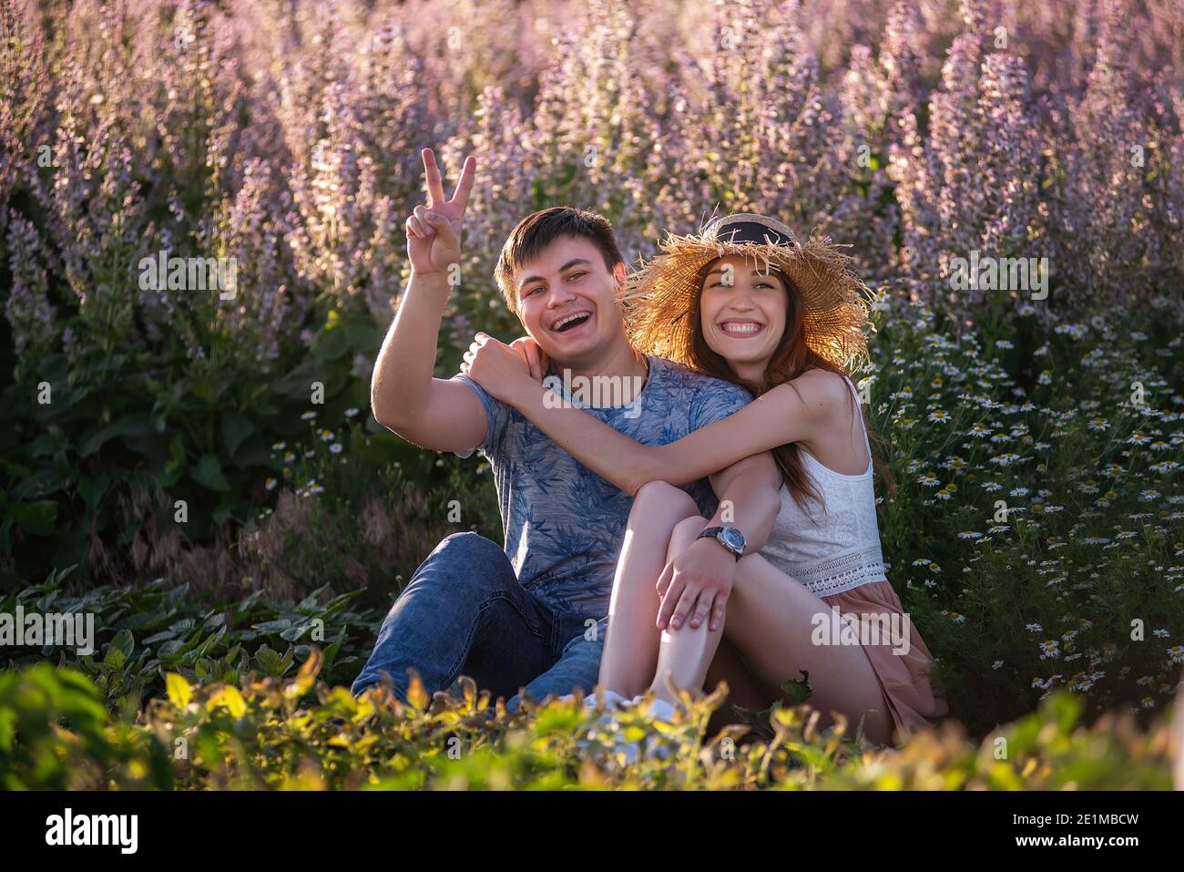 La coppia felice in amore si siede abbracciando da campo di salvia fiorente. Un giovane con bella ragazza in cappello di paglia si divertono, si imbrogliano intorno, agitando il loro ha Foto Stock