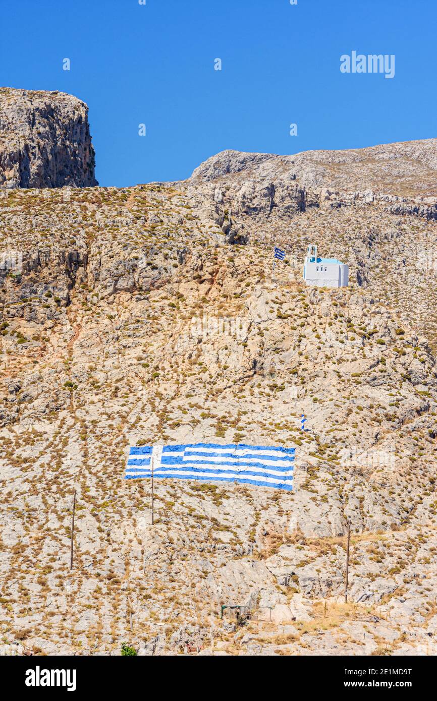 Bandiera greca e chiesa bianca sulle aride colline aride che si affacciano Kalymnos Island, Dodecanese, Grecia Foto Stock