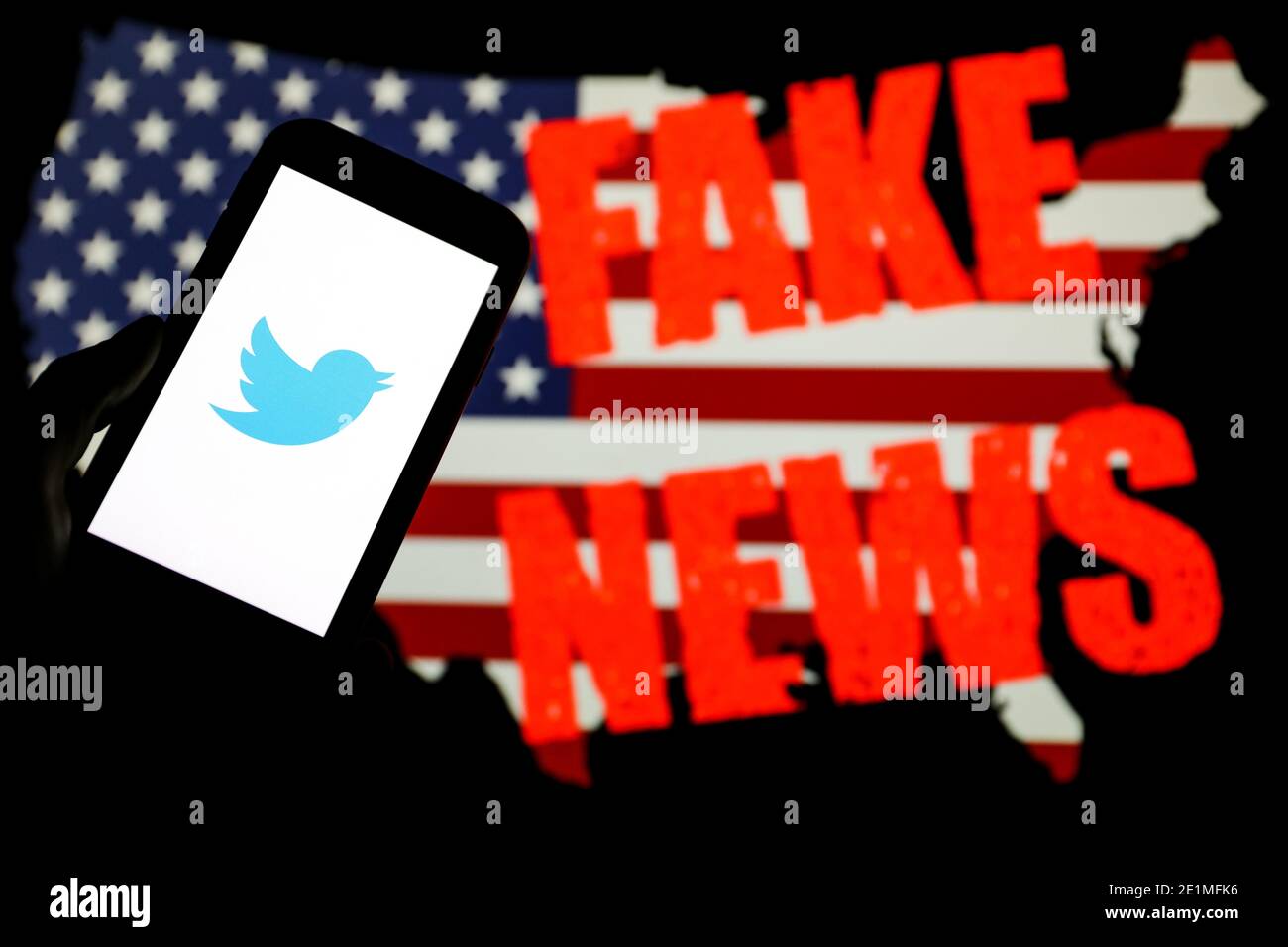 In questa illustrazione fotografica il logo dell'azienda dell'app per i social media di Twitter è visualizzato su uno smartphone. Bandiera americana con iscrizione 'Fake News' è visibile Foto Stock