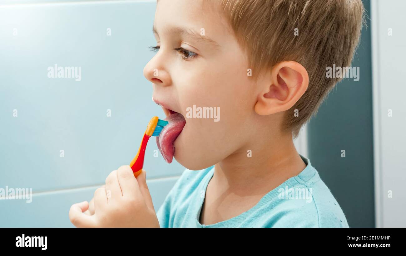 Ritratto del ragazzo che spazzola i denti e pulisce la lingua con lo spazzolino. Bambino che si prende cura dei denti e li pulisce Foto Stock