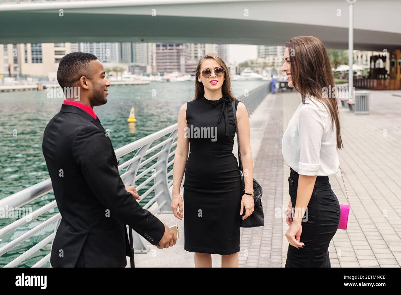 Tre uomini d'affari in piedi a Dubai Marine e chattare sui piani aziendali per il mese prossimo. Un uomo afro-americano e due donne europee in abito Foto Stock