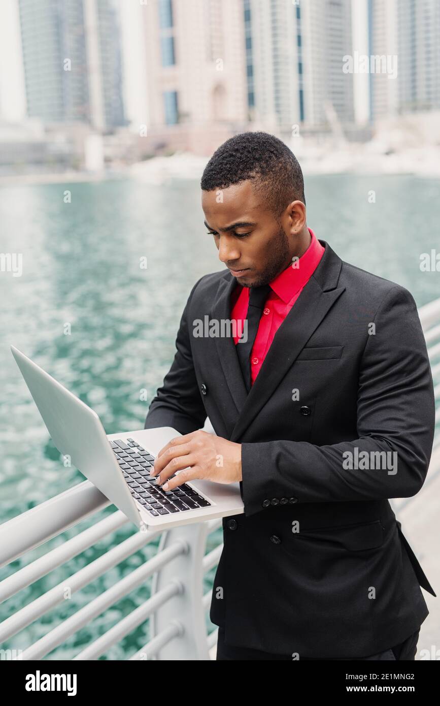Impegnato uomo d'affari afro-americano in porto e guardando attraverso alcuni documenti sul suo laptop. Foto Stock