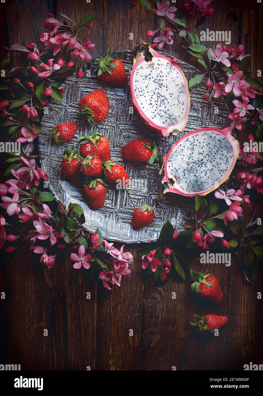 Cibo flatlay background - vuoto in legno scuro con scheda dragon frutto, fragole e fiori di colore rosa, copia spazio per il testo Foto Stock