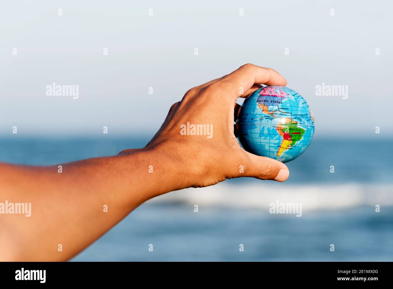 primo piano di un giovane caucasico con un globo mondiale in mano davanti all'oceano Foto Stock