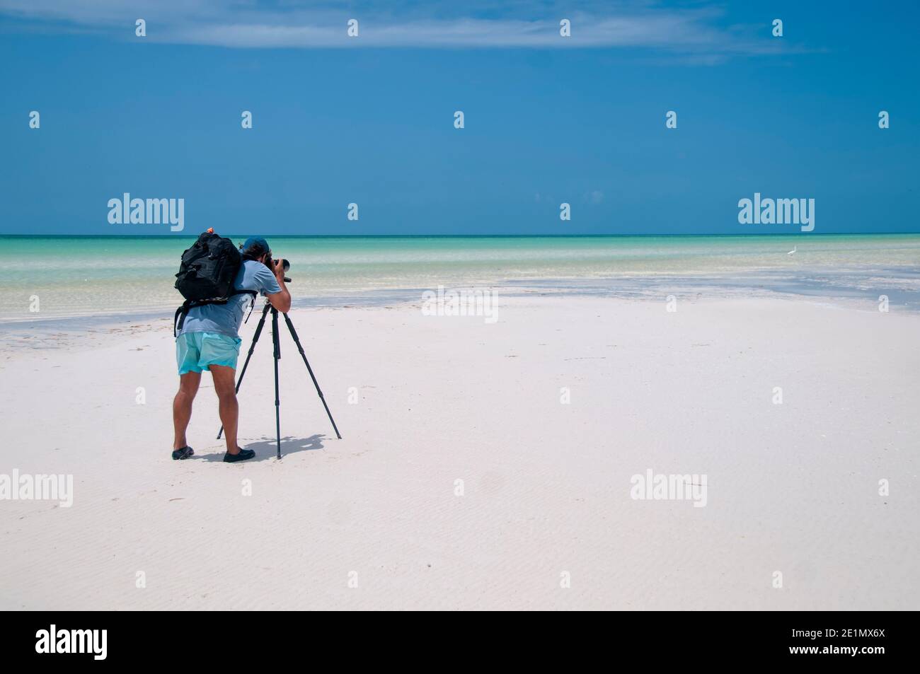Fotografo con la sua fotocamera sul suo trespolo scatta fotografie di paesaggio a bassa marea sull'isola di Holbox, Messico. Sullo sfondo il cielo blu An Foto Stock