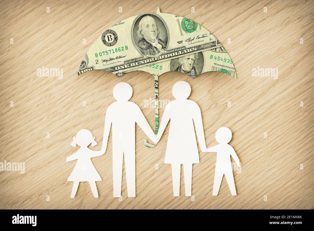 Silhouette di famiglia di carta con ombrello fatto di banconote in dollari sopra Sfondo di legno - concetto di protezione finanziaria familiare Foto Stock