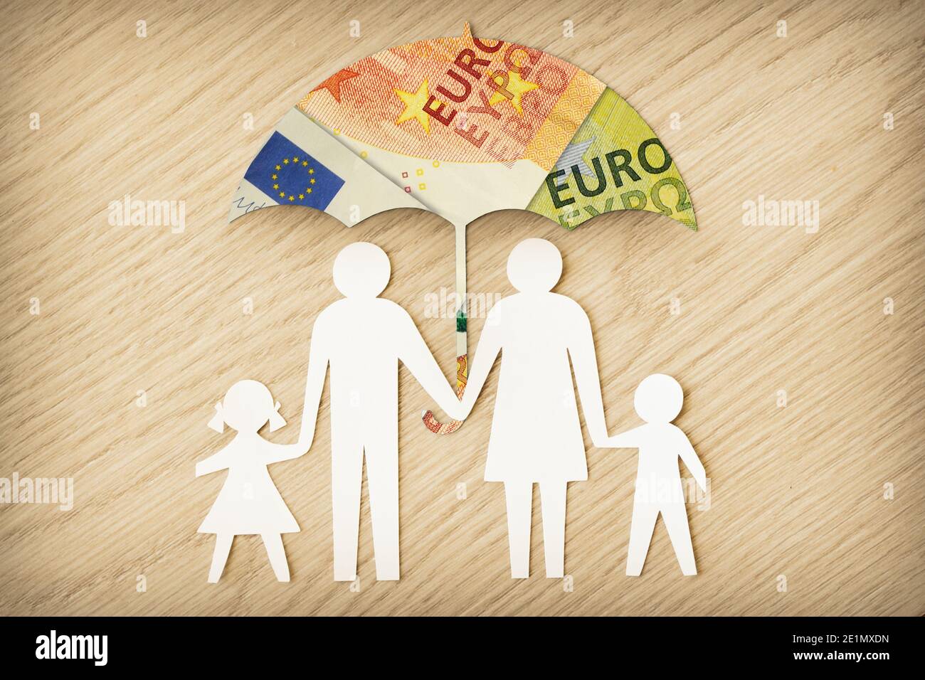 Silhouette di famiglia di carta con ombrello fatto di banconote in euro su Sfondo di legno - concetto di protezione finanziaria familiare Foto Stock