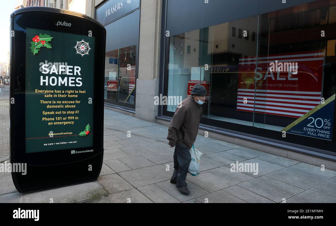 Un uomo cammina oltre un annuncio per l'operazione di saluti stagioni PSNI su una strada tranquilla nel centro di Belfast, come il blocco di sei settimane in Irlanda del Nord continua. Foto Stock