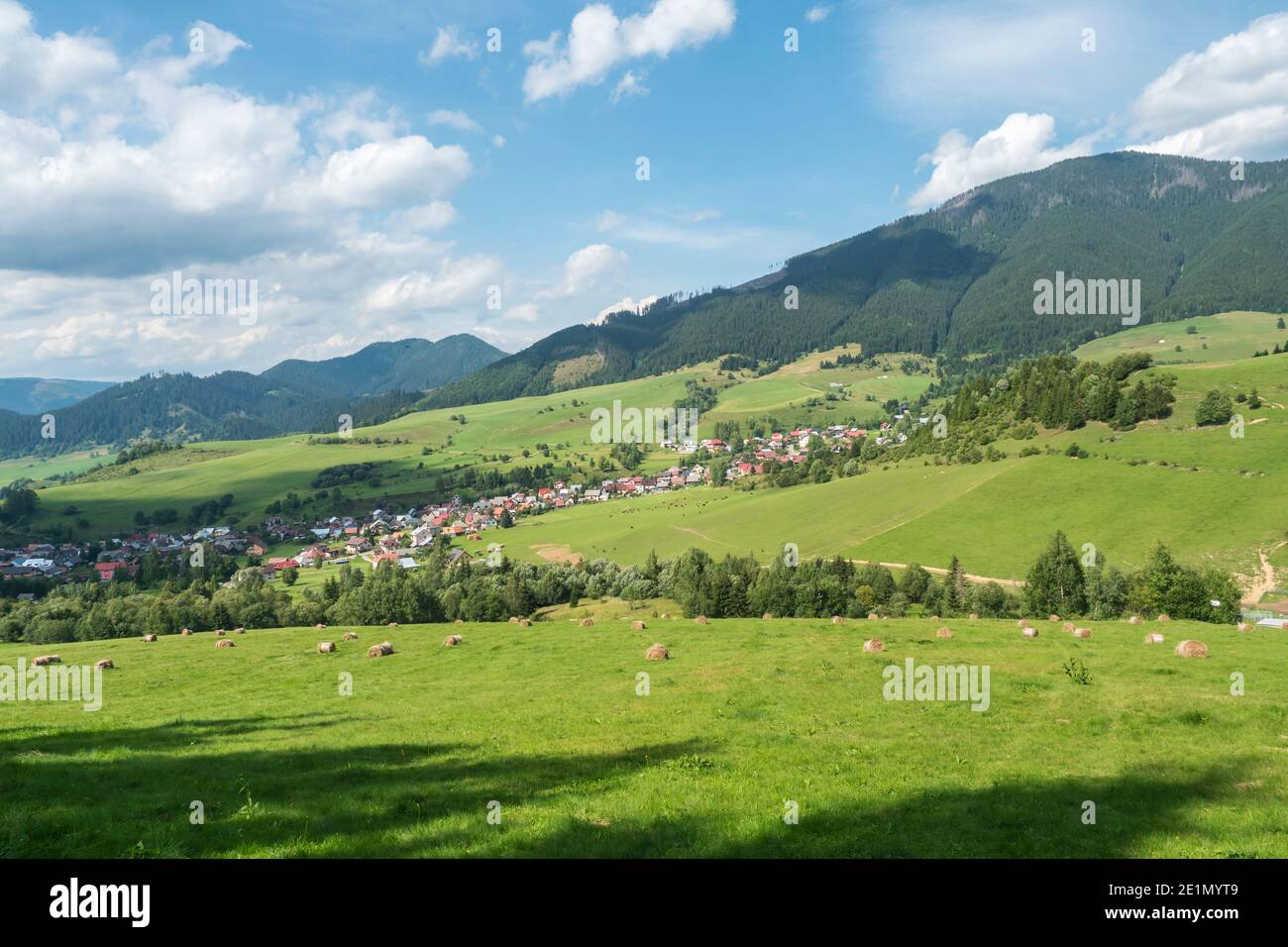 Vista sul villaggio di Liptovska Luzna ai piedi delle montagne di Low Tatra con prati verdeggianti, colline boscose e balle di paglia. Slovacchia, estate Foto Stock