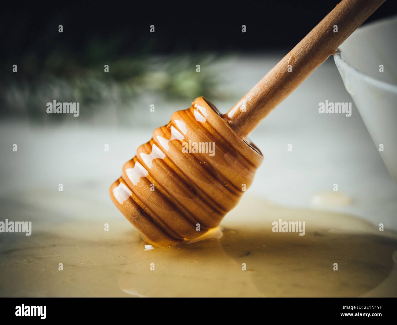 Miele su piano in marmo bianco. Il cucchiaia di legno di miele è sulla goccia di miele. Ingrediente dolce sano per cosmetici naturali, pasticceria e colazione. Oro, giallo Foto Stock