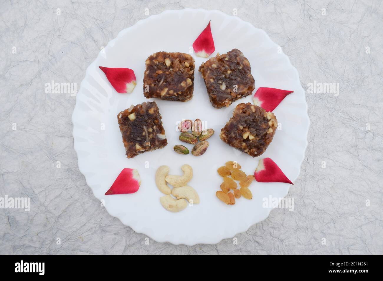 Khajur ka halwa o Khajoor paak è un piatto tradizionale indiano e pakistano. Frutta secca halwa barfi date decorate con petali di rosa rosso e serviti Foto Stock