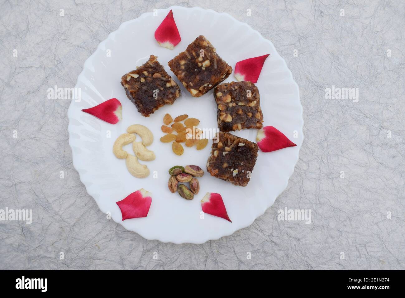 Khajur ka halwa o Khajoor paak è un piatto tradizionale indiano e pakistano. Frutta secca halwa barfi date decorate con petali di rosa rosso e serviti Foto Stock