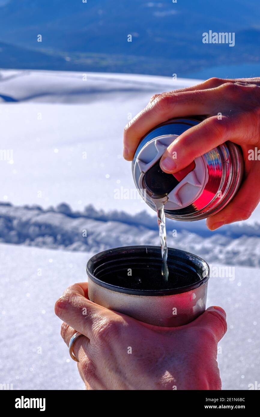 Versare il tè da una fiasca sulla cima di una montagna su un paesaggio innevato Foto Stock