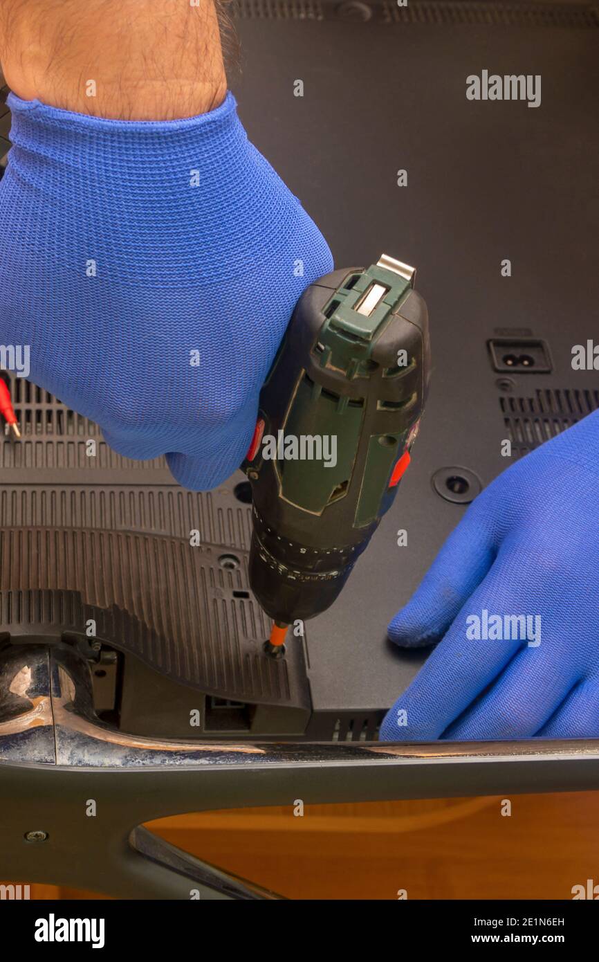 Un tecnico del centro di assistenza svita il pannello posteriore di un televisore LCD utilizzando un cacciavite. Mani in guanti primo piano, messa a fuoco selettiva. Foto Stock