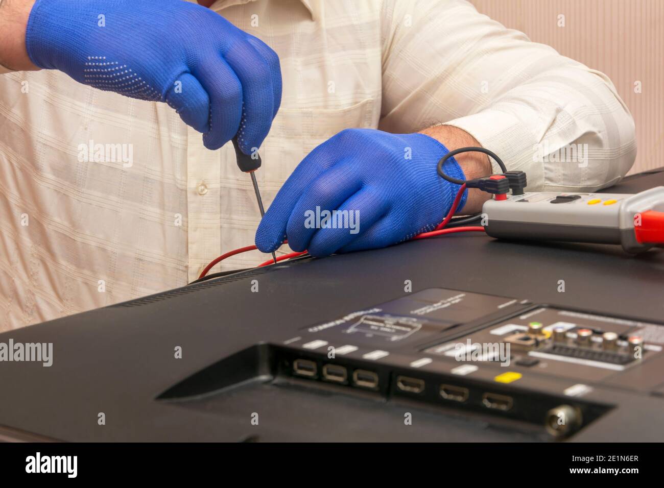 La riparazione del televisore LCD, il tecnico dei guanti con un cacciavite rimuove il pannello posteriore del monitor. Messa a fuoco selettiva, primo piano. Foto Stock
