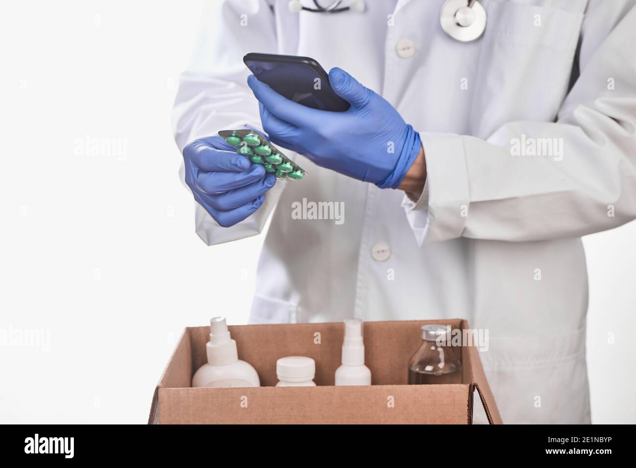 Medico che raccoglie i medicinali prescritti in una scatola e utilizzando un telefono Foto Stock