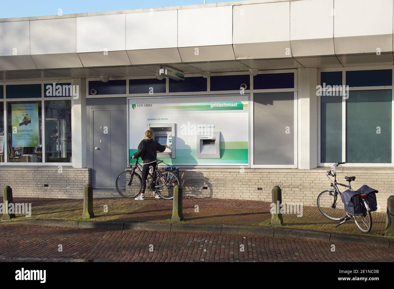 Olanda, Bergen, 8 gennaio 2021. Signora con una bicicletta su un cashpoint (bancomat, bancomat, bancomat) della banca olandese ABN-AMRO. Foto Stock