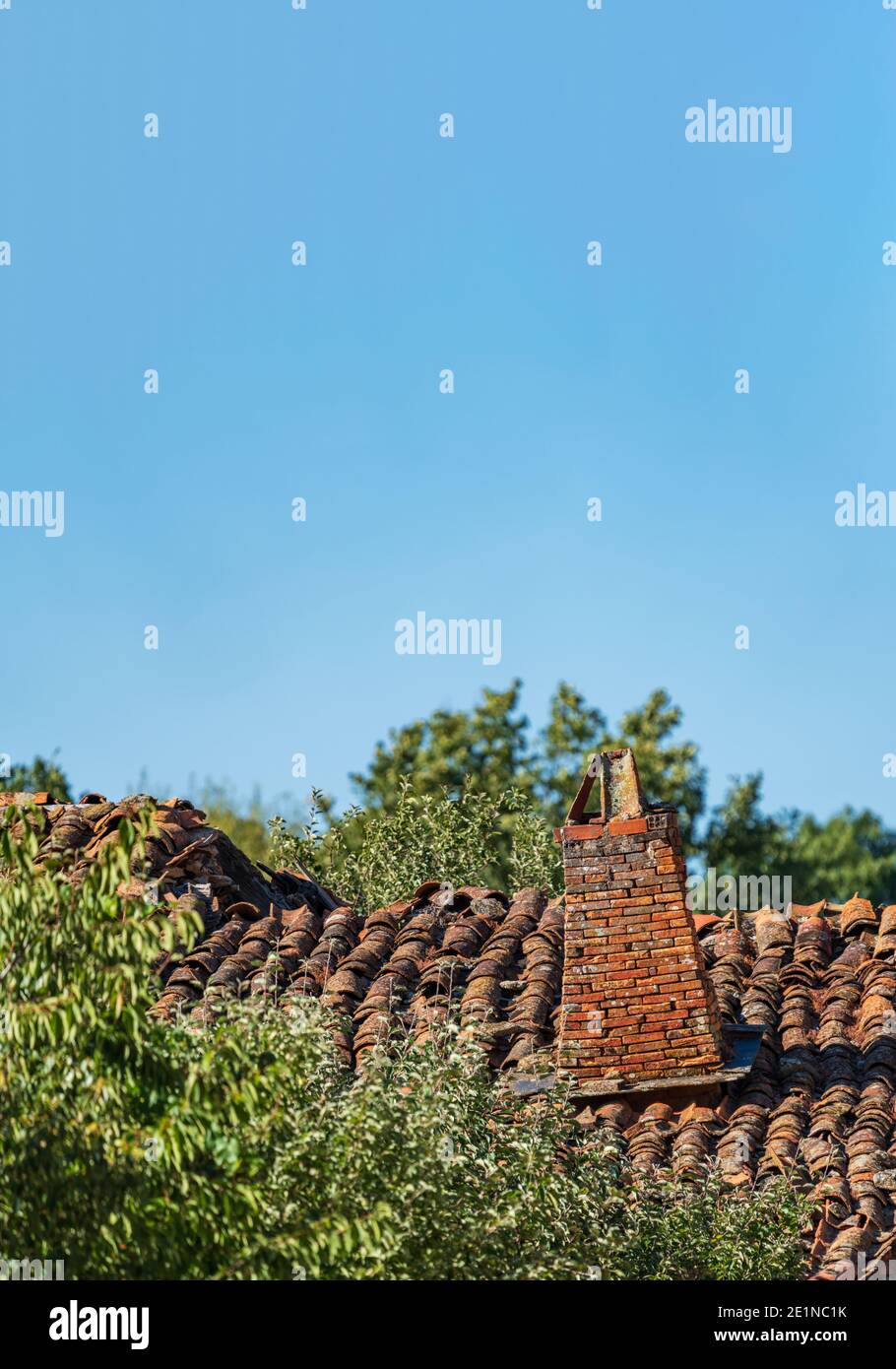 Camino d'epoca sopra il tetto di tegole stucchiato sotto il cielo blu Foto Stock