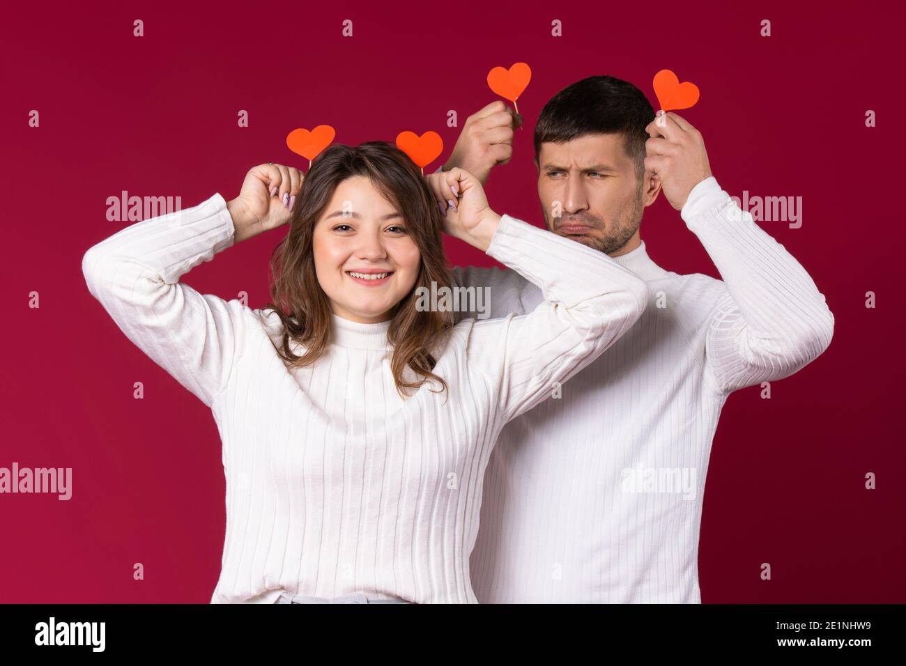 Una giovane coppia si sta imbrogliando su uno sfondo rosso con cuori di cartone fatti a mano. Passatempo il giorno di San Valentino. Foto Stock