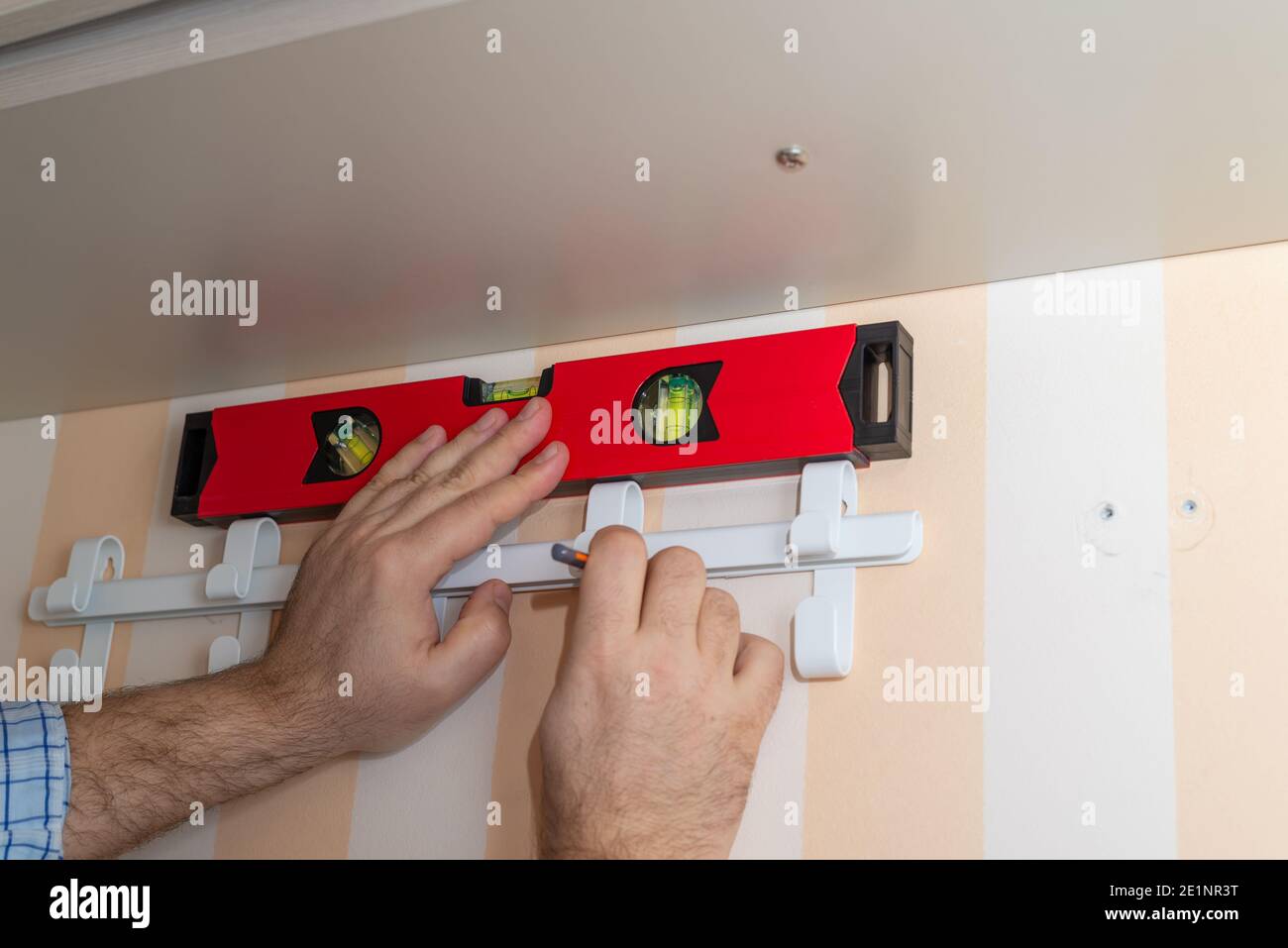 Uomo che segna una posizione di ganci armadio con una bolla strumento di livello Foto Stock